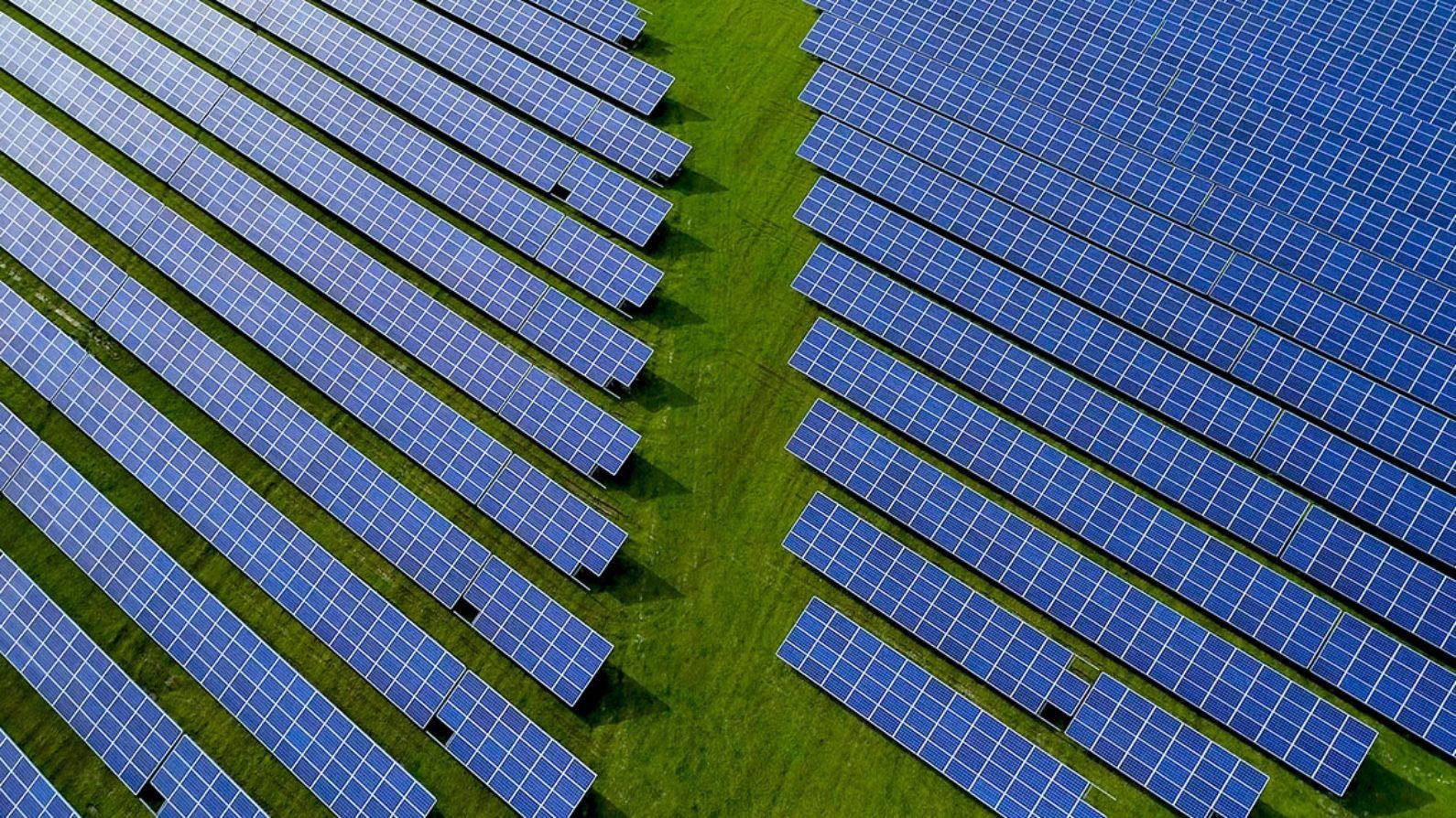 Aerial view of rows of solar panels on green pasture